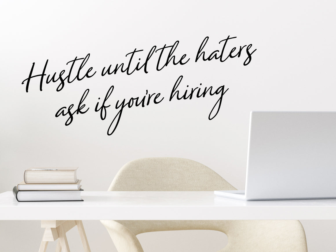 Wall decal for the office that says ‘Hustle Until The Haters Ask If You're Hiring’ in a cursive font on an office wall.