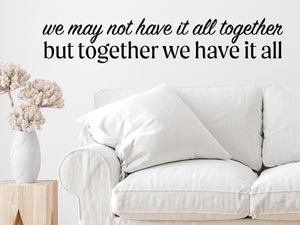 Living room wall decals that say ‘We May Not Have It All Together But Together We Have It All’ in a script font on a living room wall. 