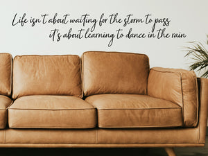 Living room wall decals that say ‘Life Isn't About Waiting For The Storm To Pass’ in a cursive font on a living room wall. 