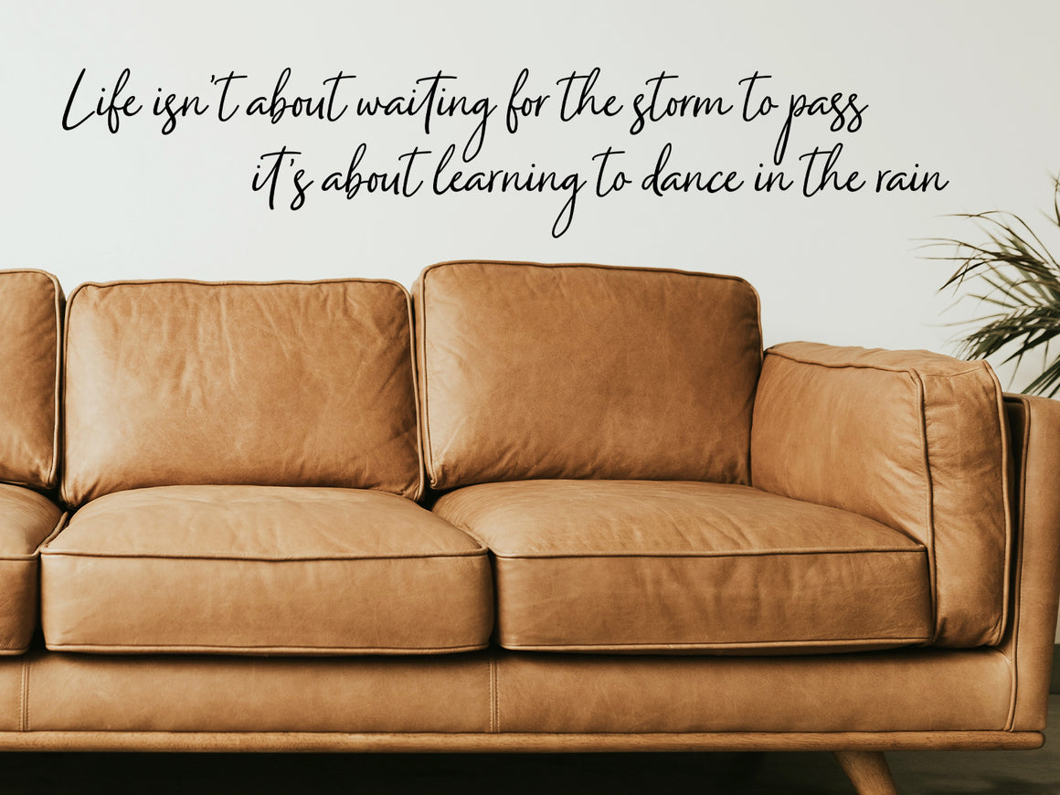 Living room wall decals that say ‘Life Isn't About Waiting For The Storm To Pass’ in a cursive font on a living room wall. 