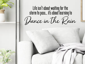 Living room wall decals that say ‘Life Isn't About Waiting For The Storm To Pass’ in a script font on a living room wall. 