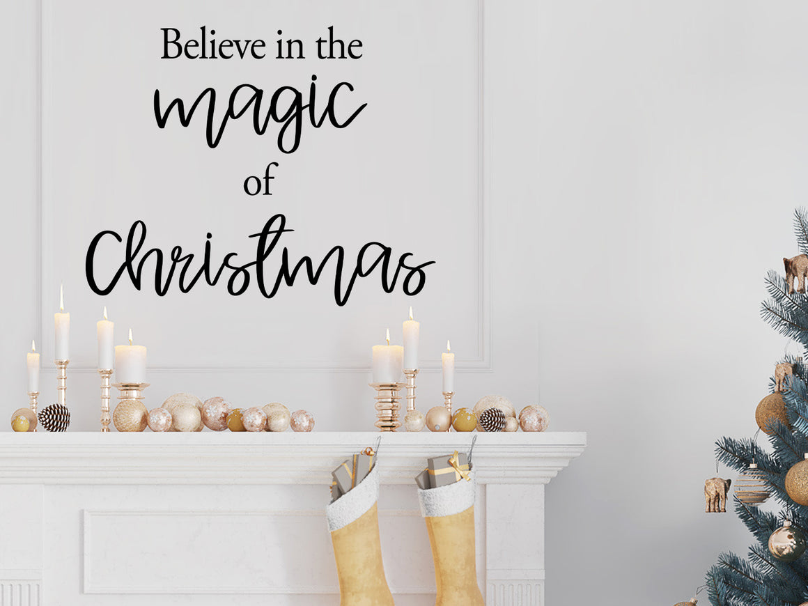 Living room wall decals that say ‘Believe In The Magic Of Christmas’ in a cursive font on a living room wall. 