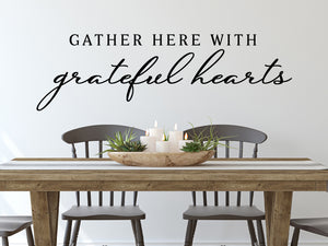 Wall decals for kitchen that say ‘Gather Here With Grateful Hearts’ in a script font on a kitchen wall.