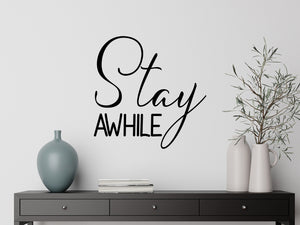 Living room wall decals that say ‘Stay Awhile’ in a script font on a living room wall. 
