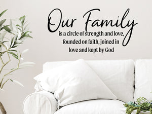 Living room wall decals that say ‘Our Family Is A Circle Of Strength And Love’ in a script font on a living room wall. 