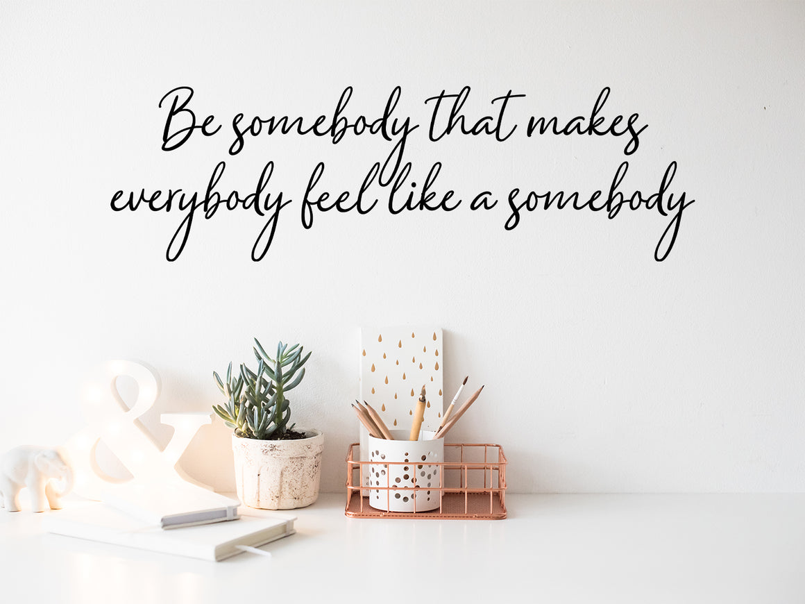 Wall decal for the office that says ‘Be Somebody That Makes Everybody Feel Like A Somebody’ in a cursive font on an office wall.