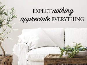 Living room wall decals that say ‘Expect Nothing Appreciate Everything’ in a script font on a living room wall.
