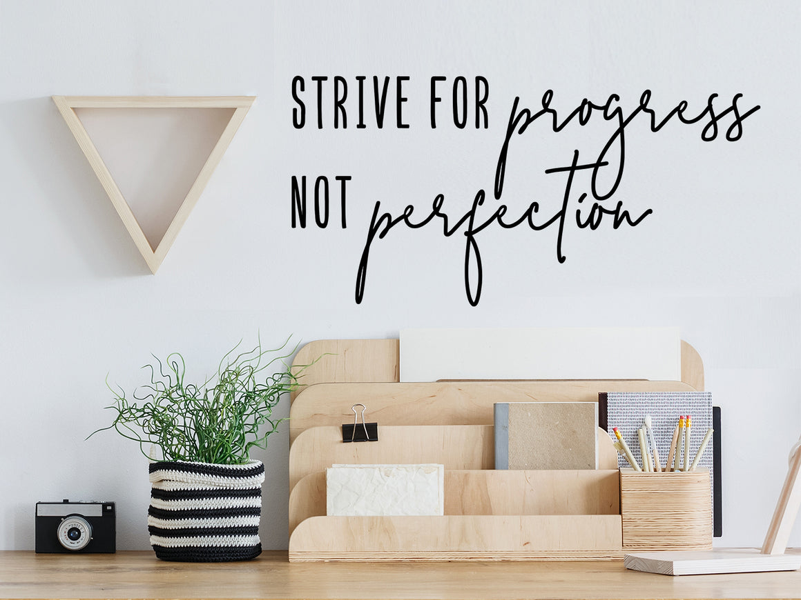 Decorative wall decal that says ‘Strive For Progress Not Perfection’ on an office wall.
