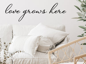 Living room wall decals that say ‘Love Grows Here’ in a cursive font on a living room wall. 