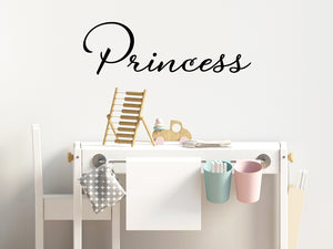 Wall decal for kids that says ‘Princess’ in black in a cursive font on a kid’s room wall. 