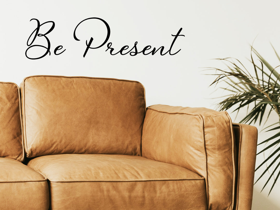 Living room wall decals that say ‘Be Present’ in a cursive font on a living room wall. 