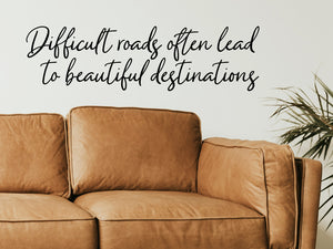 Living room wall decals that say ‘Difficult Roads Often Lead To Beautiful Destinations’ in a script font on a living room wall.