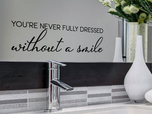 Wall decals for bathroom that say ‘You're Never Fully Dressed Without A Smile’ in a cursive font on a bathroom mirror.