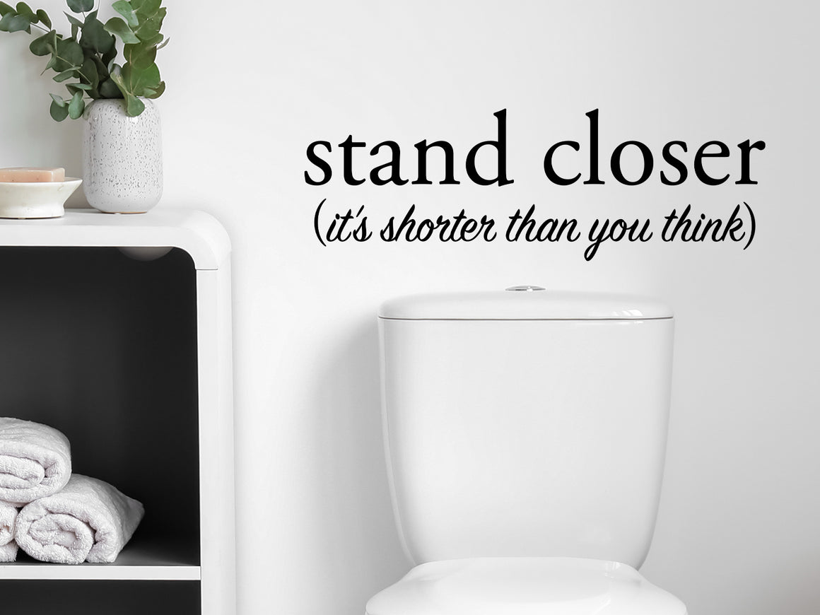 Wall decals for bathroom that say ‘Stand Closer It's Shorter Than You Think’ in a cursive font on a bathroom wall.