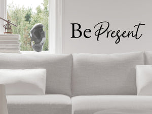 Living room wall decals that say ‘Be Present’ in a script font on a living room wall. 