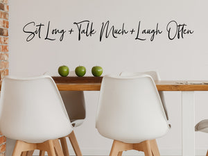 Wall decals for kitchen that say ‘Sit Long Talk Much Laugh Often’ in a script font on a kitchen wall.