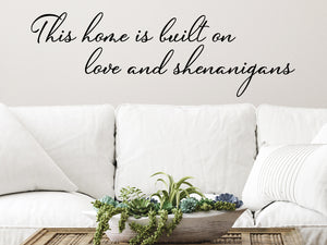 Living room wall decals that say ‘This Home Is Built On Love And Shenanigans’ in a cursive font on a living room wall. 