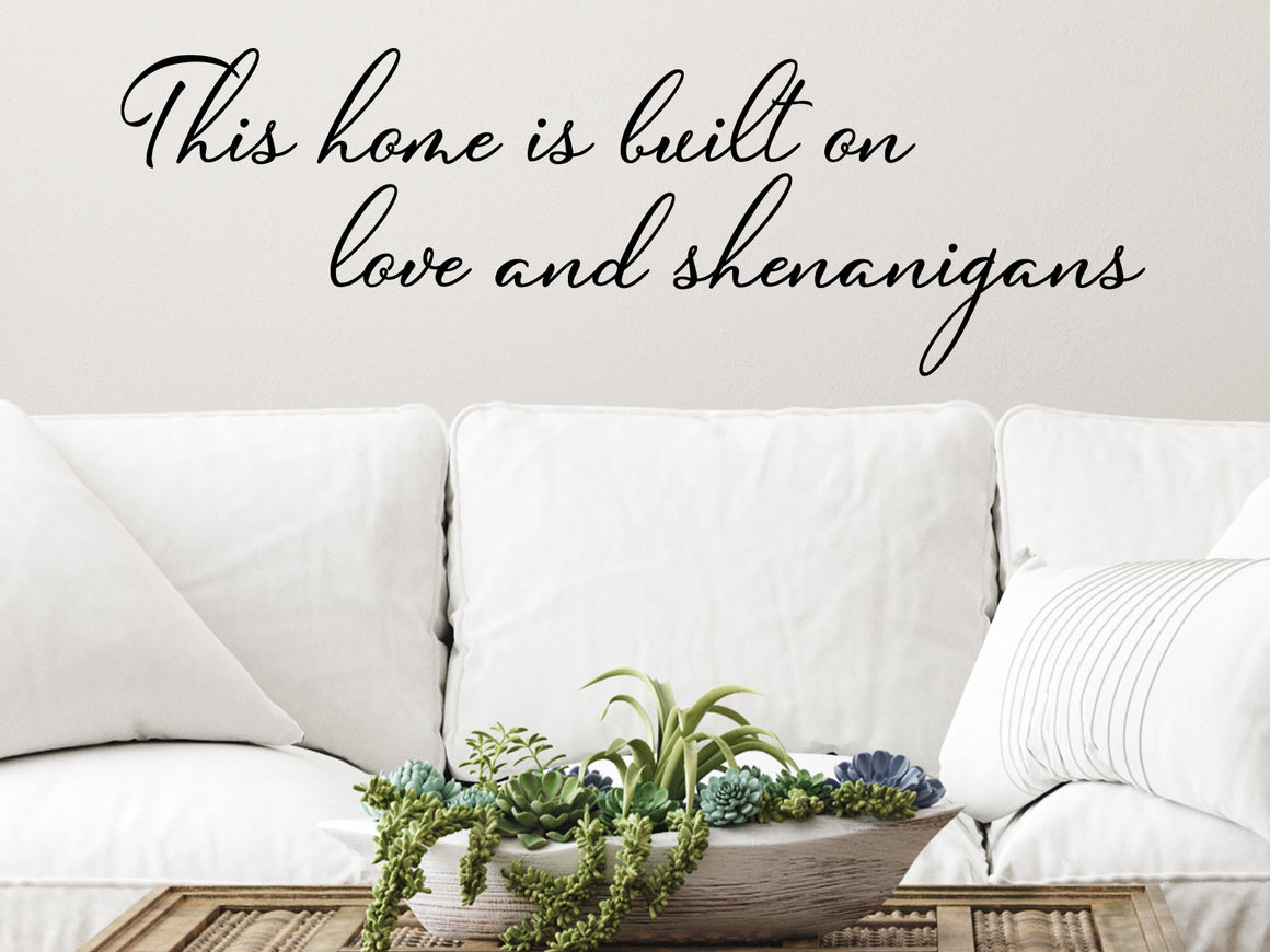 Living room wall decals that say ‘This Home Is Built On Love And Shenanigans’ in a cursive font on a living room wall. 