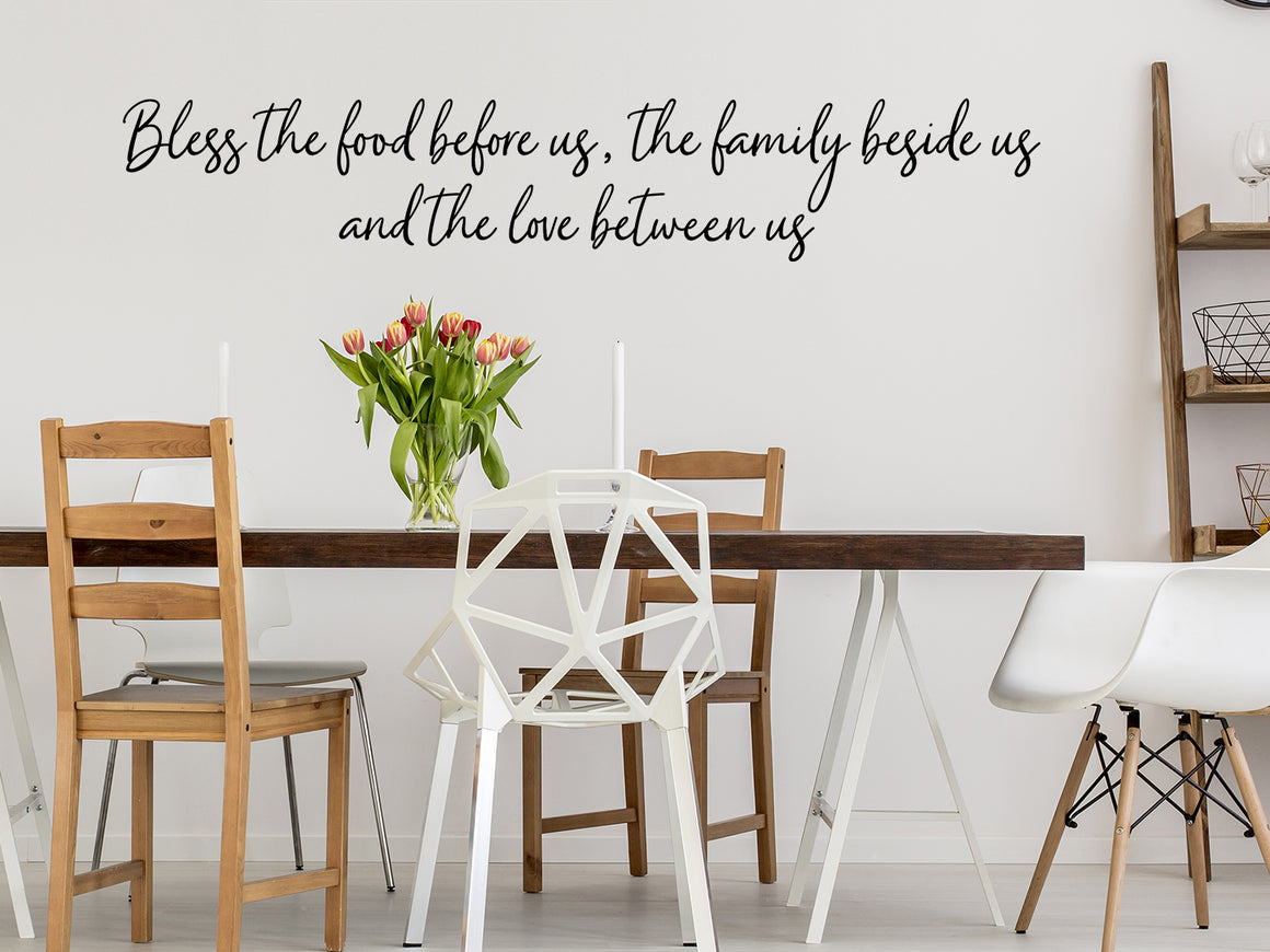 Wall decals for kitchen that say ‘Bless The Food Before Us The Family Beside Us And The Love Between Us’ in a cursive font on a kitchen wall.
