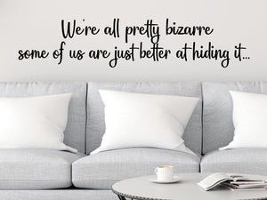 Living room wall decals that say ‘We're all pretty bizarre some of us are just better at hiding it’ in a script font on a living room wall. 