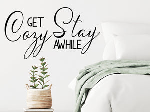 Wall decal for bedroom that says ‘get cozy stay awhile’ on a bedroom wall.