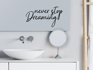 Wall decals for bathroom that say ‘Never Stop Dreaming’ in a cursive font on a bathroom mirror.