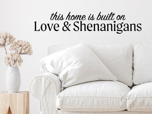 Living room wall decals that say ‘This Home Is Built On Love And Shenanigans’ in a bold font on a living room wall. 