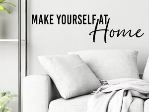 Living room wall decals that say ‘Make Yourself At Home’ in a script font on a living room wall. 