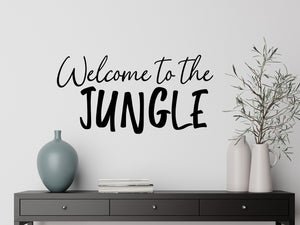 Living room wall decals that say ‘Welcome To The Jungle’ in a cursive font on a living room wall. 