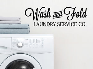 Laundry room wall decal that says ‘Wash And Fold Laundry Service Co.’ in a script font on a laundry room wall.