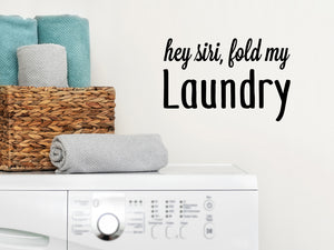 Laundry room wall decal that says ‘Hey Siri Fold My Laundry’ in a script font on a laundry room wall