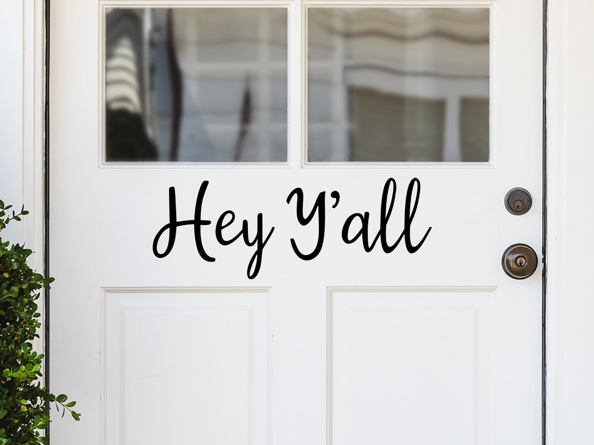 Front door decal that says, ‘Hey Ya’ll’ in a cursive font on a front porch door. 