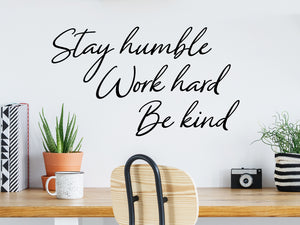 Wall decal for the office that says ‘Stay Humble Work Hard Be Kind’ in a cursive font on an office wall.