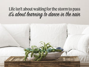 Living room wall decals that say ‘Life Isn't About Waiting For The Storm To Pass’ in a bold font on a living room wall. 