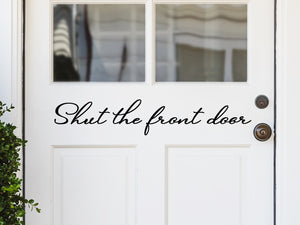 Front door decal that says, ‘Shut the front door’ in a script font  on a front porch door. 