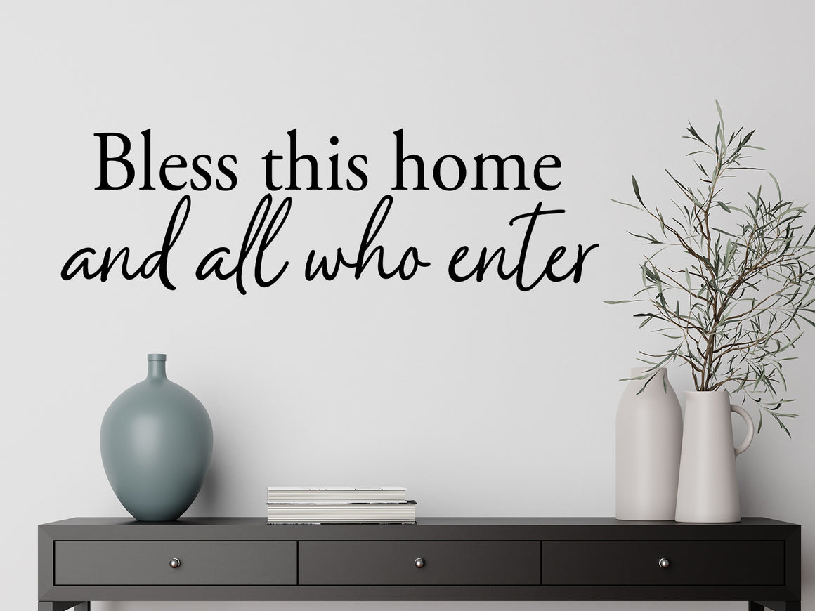 Living room wall decals that say ‘Bless This Home And All Who Enter’ in a script font on a living room wall. 