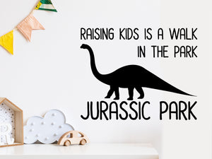 Wall decal for kids that says ‘raising kids is a walk in the park, Jurassic Park’ on a kid’s room wall. 