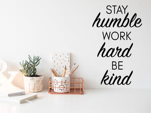 Wall decal for the office that says ‘Stay Humble Work Hard Be Kind’ in a bold font on an office wall.