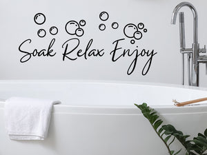 Wall decals for bathroom that say ‘Soak Relax Enjoy Bubbles’ in a cursive font on a bathroom wall.