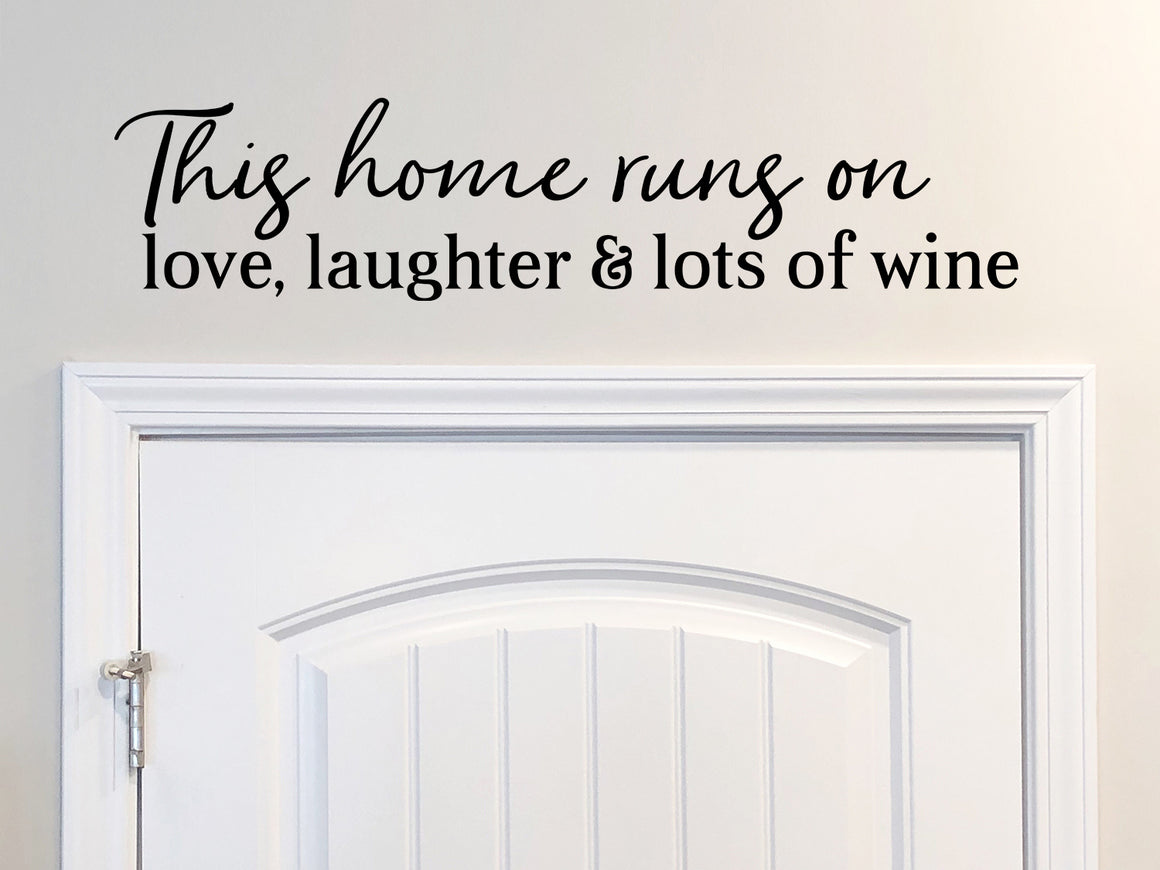 Wall decals for kitchen that say ‘This House Runs On Love Laughter And Lots Of Wine’ in a script font on a kitchen wall.