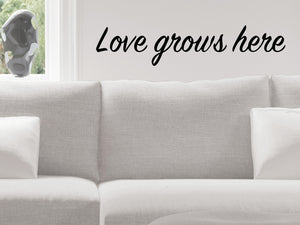 Living room wall decals that say ‘Love Grows Here’ in a script font on a living room wall. 