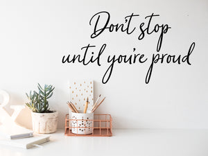 Wall decal for the office that says ‘Don't Stop Until You're Proud’ in a cursive font on an office wall.