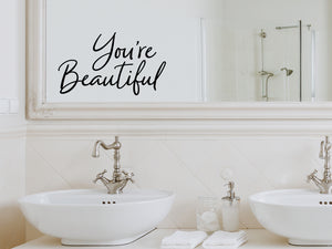 Wall decals for bathroom that say ‘You're Beautiful’ in a cursive font on a bathroom mirror.