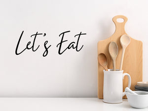 Wall decals for kitchen that say ‘let's eat’ in a script font on a kitchen wall.