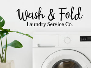 Laundry room wall decal that says ‘Wash And Fold Laundry Service Co.’ in a cursive font on a laundry room wall.