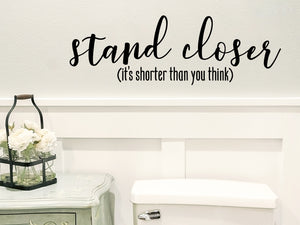 Wall decals for bathroom that say ‘stand closer it's shorter than you think’ on a bathroom wall.