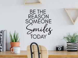 Wall decal for the office that says ‘Be The Reason Someone Smiles Today’ in a print font on an office wall.
