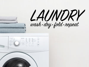 Laundry room wall decal that says ‘Laundry Wash Dry Fold Repeat’ in a cursive font on a laundry room wall.