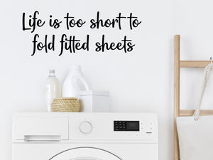 Laundry room wall decal that says ‘Life Is Too Short To Fold Fitted Sheets’ in a script font on a laundry room wall