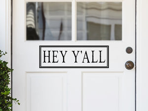 Front door decal that says, ‘Hey Ya’ll’ with a decorative square around it on a front porch door. 